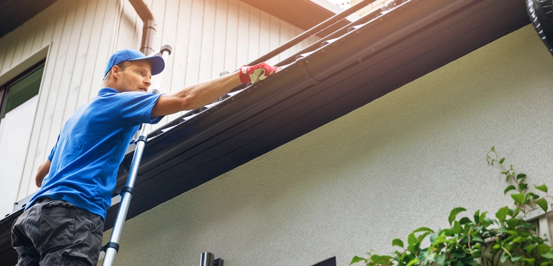 A man , standing on a ladder, cleaning his home gutters